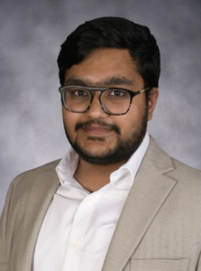 A man smiles lightly while wearing glasses. 